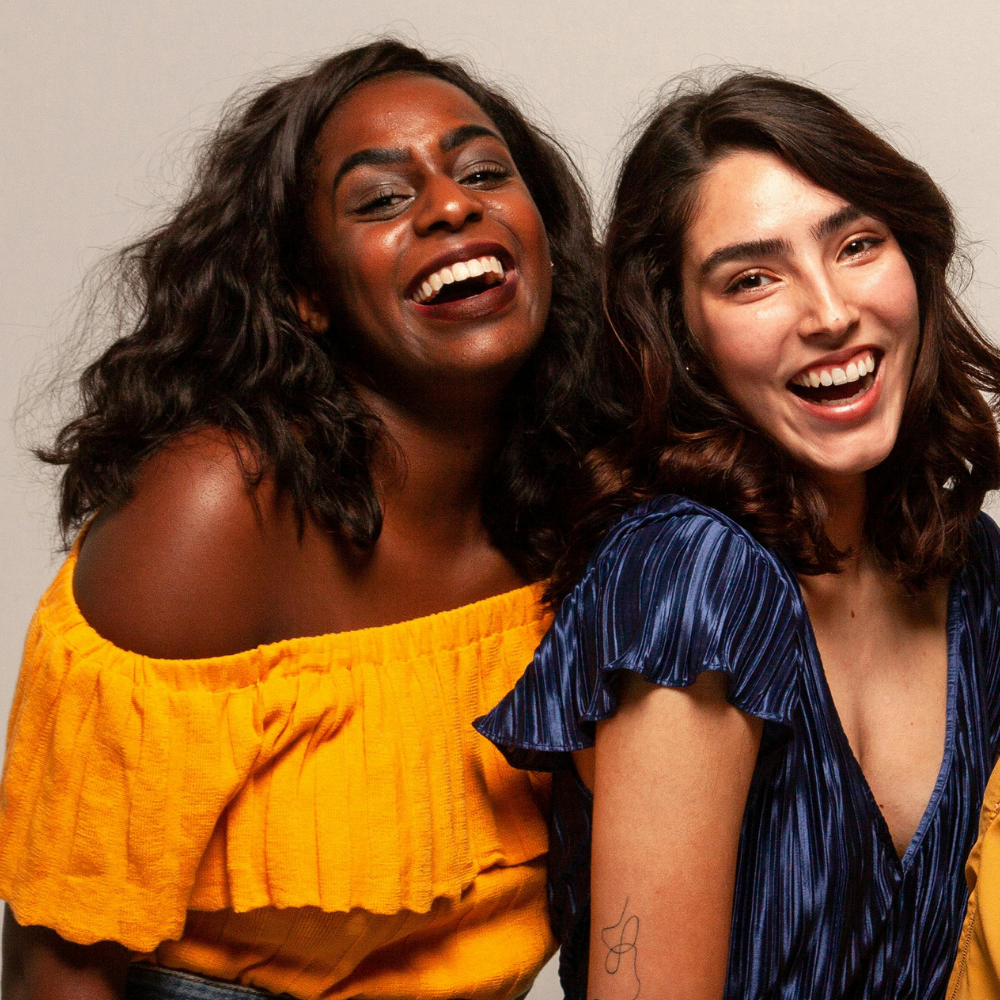 Two women laughing together, one in a yellow top and the other in a blue top.